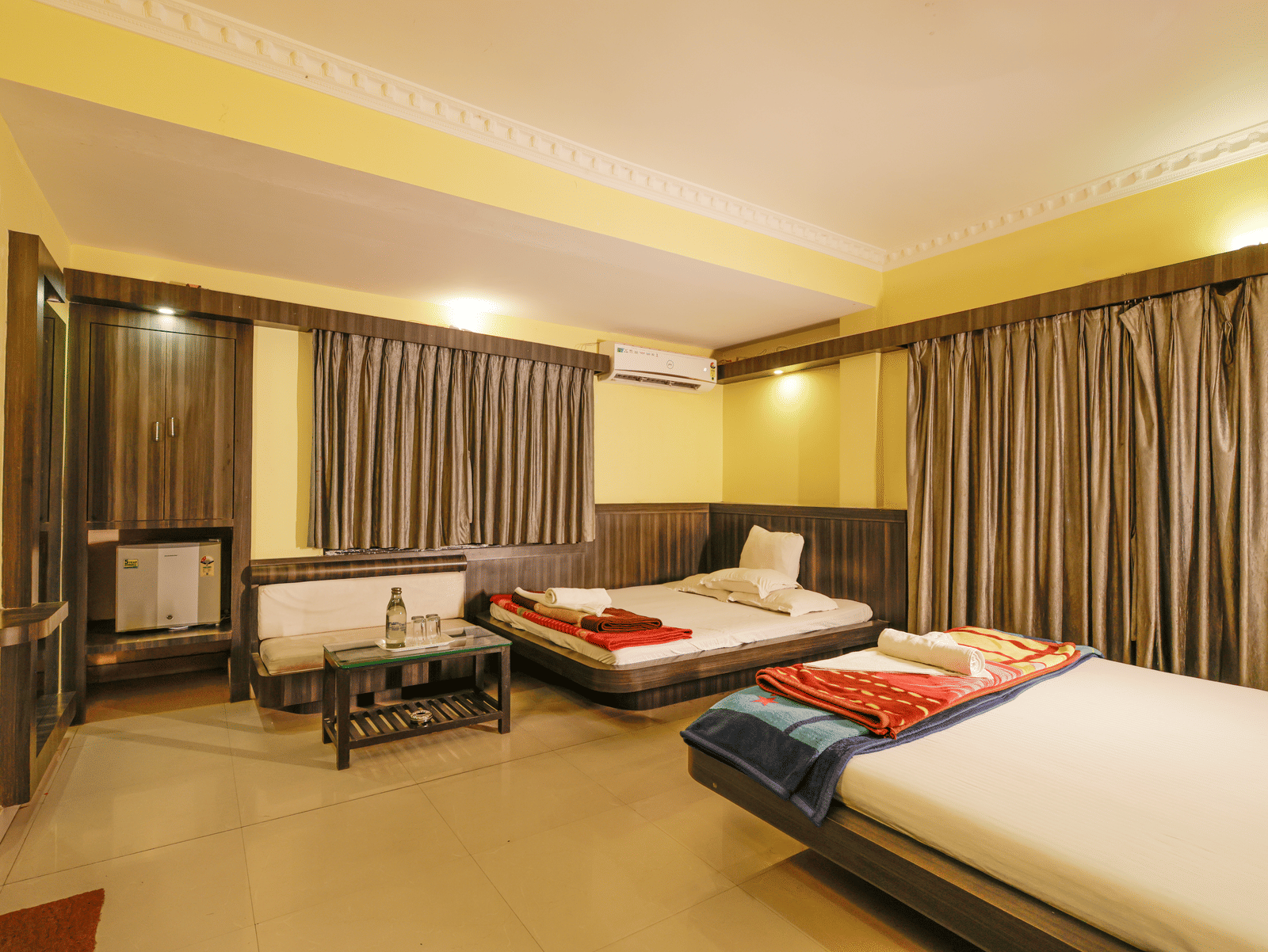 A bedroom with 2 king beds, a sofa, a coffee table, a mini fridge, curtains, and a wardrobe at Hotel Seagull Digha.